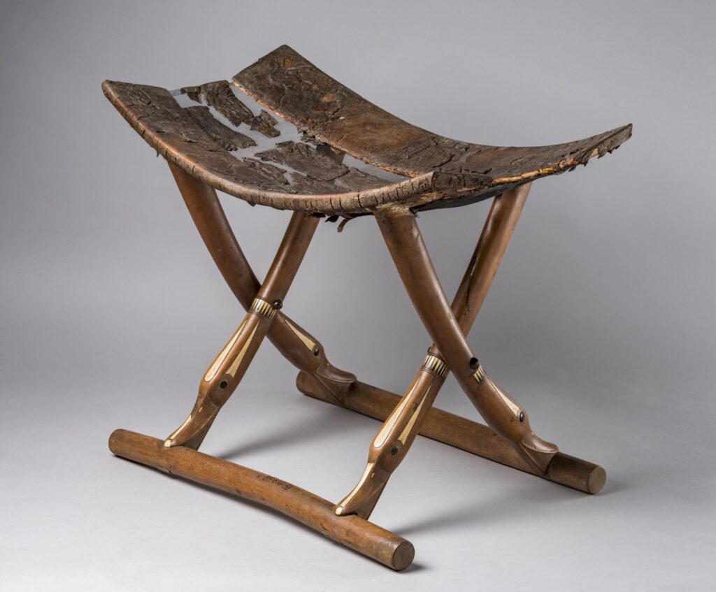 Ancient Egyptian folding stool with curved wooden seat, mortise and tenon joints, and decorative inlays