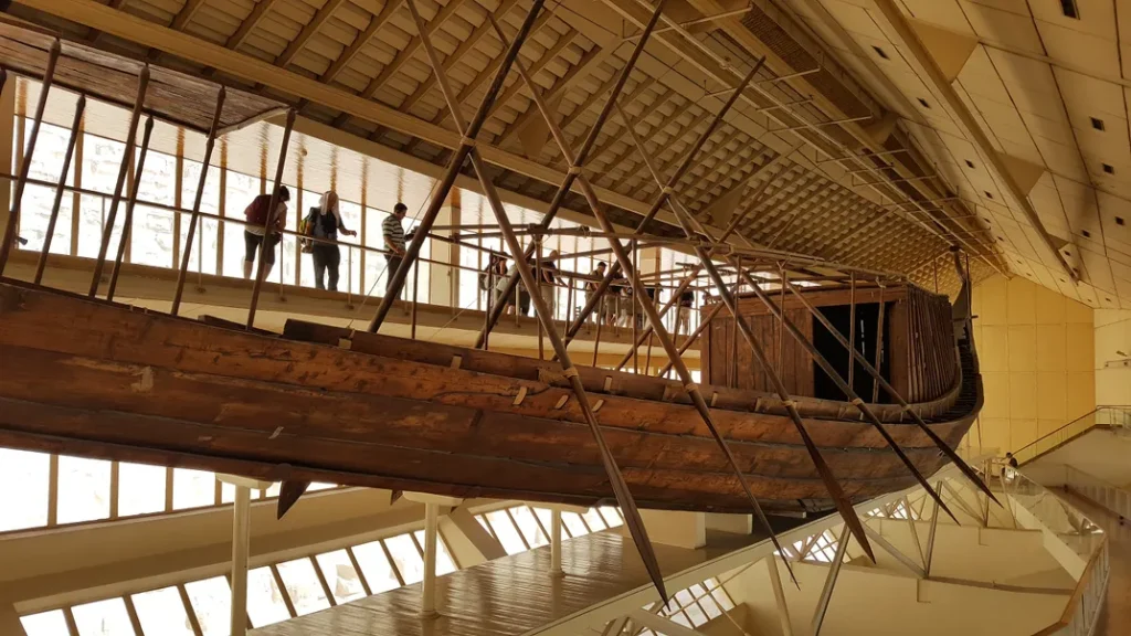 The reconstructed ancient Khufu ship displayed at the Giza Solar Boat Museum, showing visitors walking alongside the massive wooden vessel